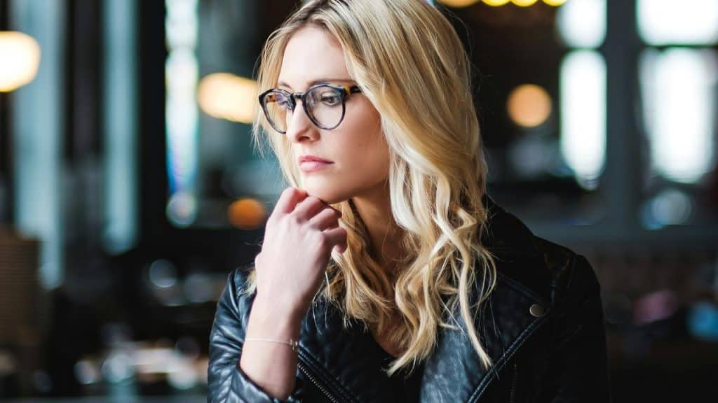 A woman wearing glasses looking thoughtful while resting her chin on her hand