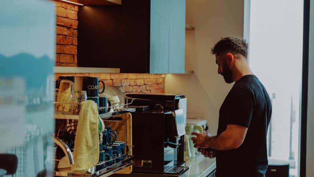 A man stands in a kitchen preparing coffee at a machine.