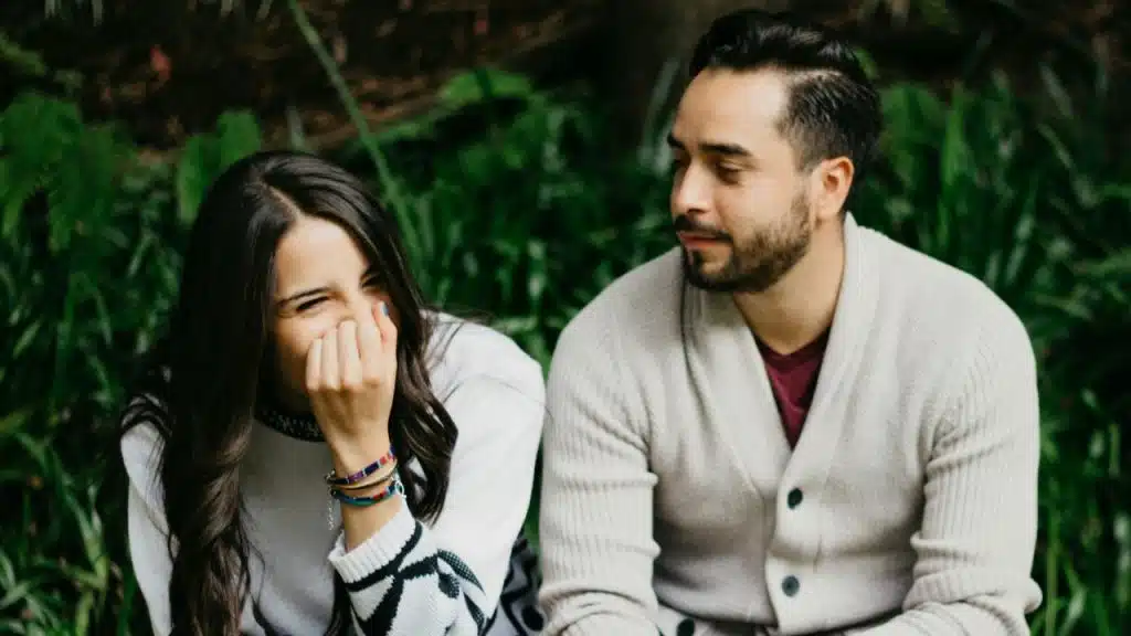 A woman laughing with her hand over her face sitting next to a bearded man.