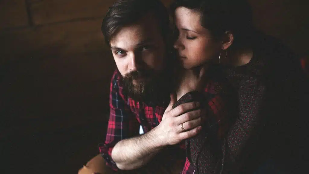 A woman leans her head against a bearded man wearing a red plaid shirt.