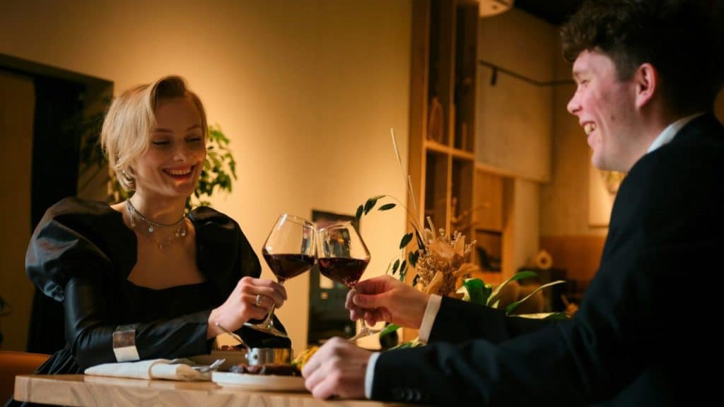 A man and woman smile while clinking wine glasses together during a dinner date.