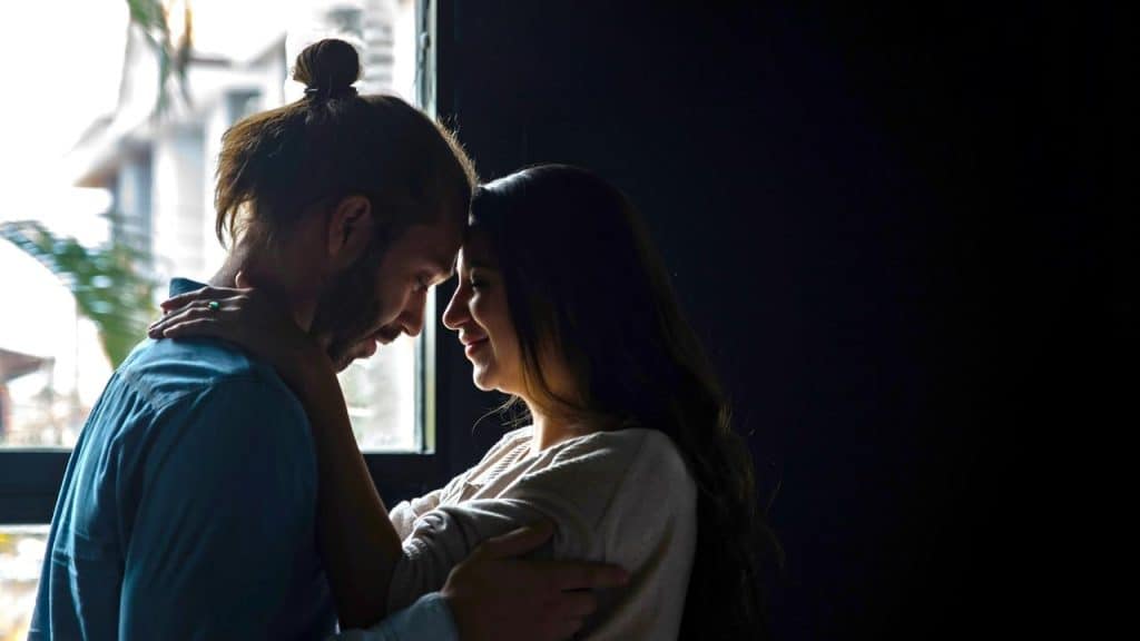 A couple standing close with foreheads touching, sharing an intimate moment.