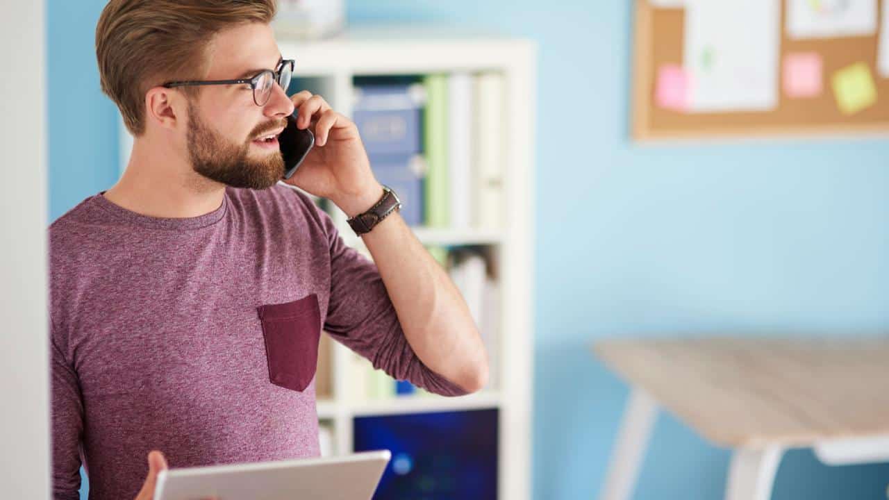 A man holding a tablet while talking on a phone in an office.