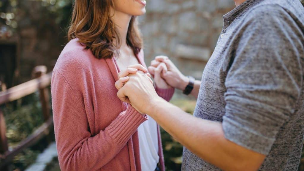 A couple holding hands and facing each other outdoors.