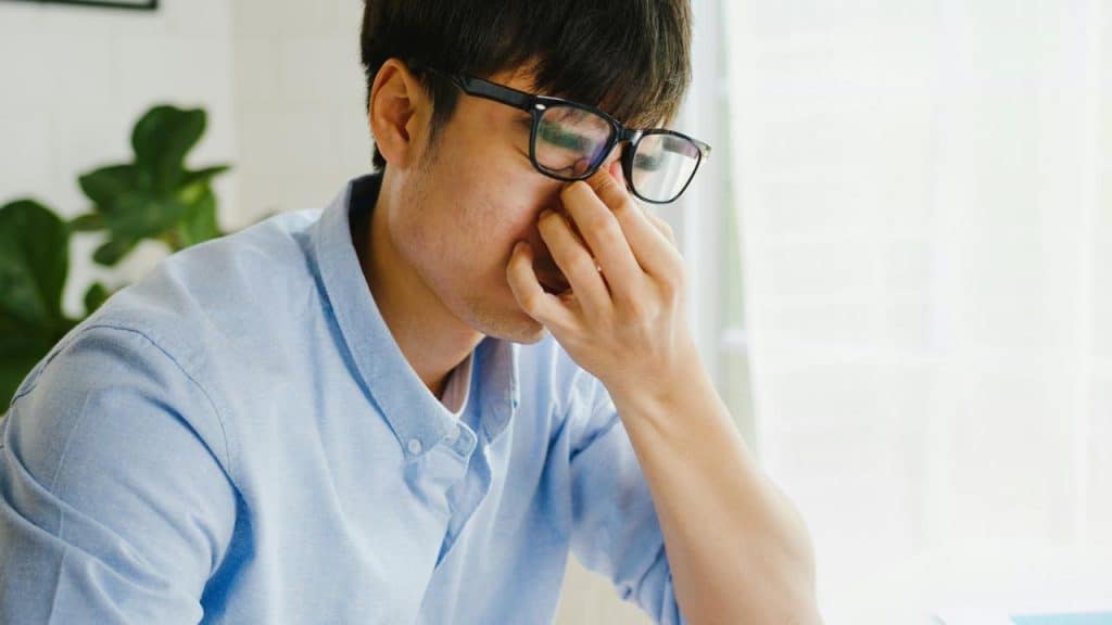 A man in glasses pinches the bridge of his nose looking stressed.