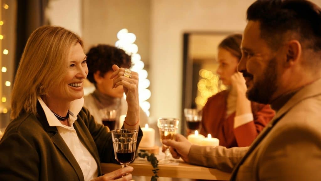A smiling woman holds a wine glass while talking to a man at a dinner.