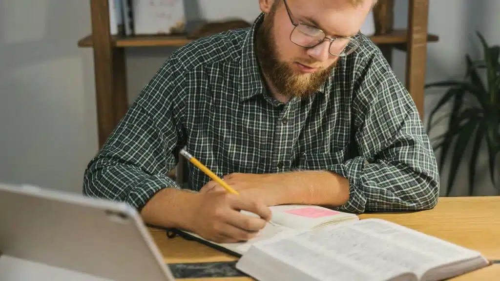 A man studying at a desk with an open book and notebook.