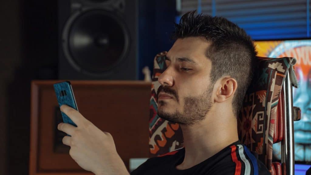 A lightly bearded man looking at his phone with an inscrutable expression. 
