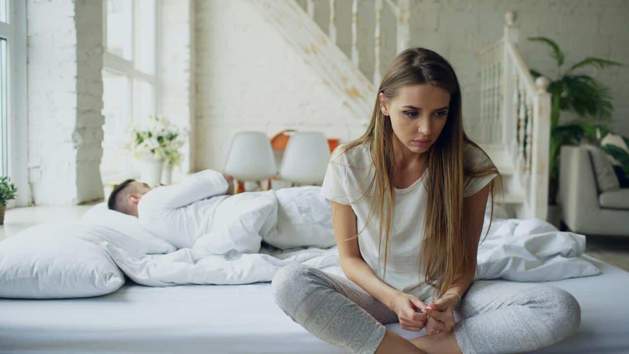 A woman sits on a bed looking down