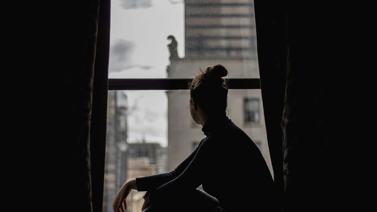 A person sitting in silhouette by a window, looking out at city buildings.