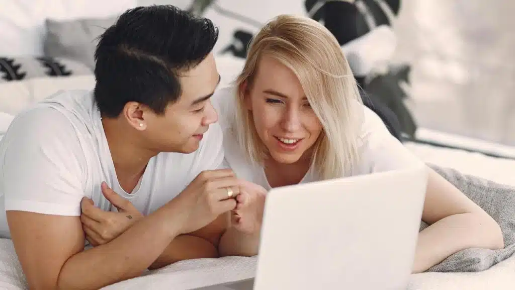 A couple lying on a bed and looking at a laptop