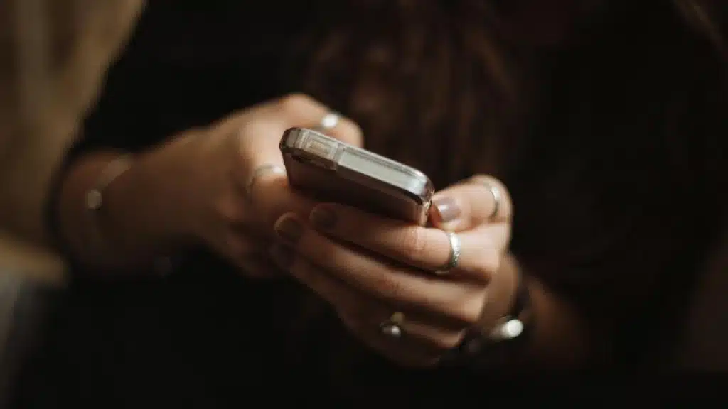 A close-up shot of a person's hands, adorned with several silver rings, holding and using a smartphone.