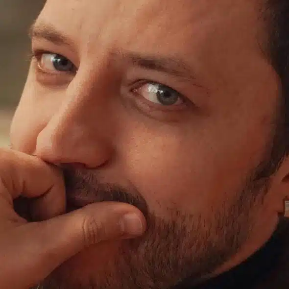 A man rests his hand near his mouth while looking thoughtful.