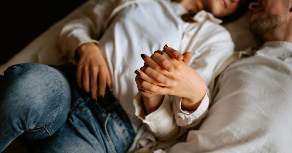 A couple lying together while holding hands on a bed.