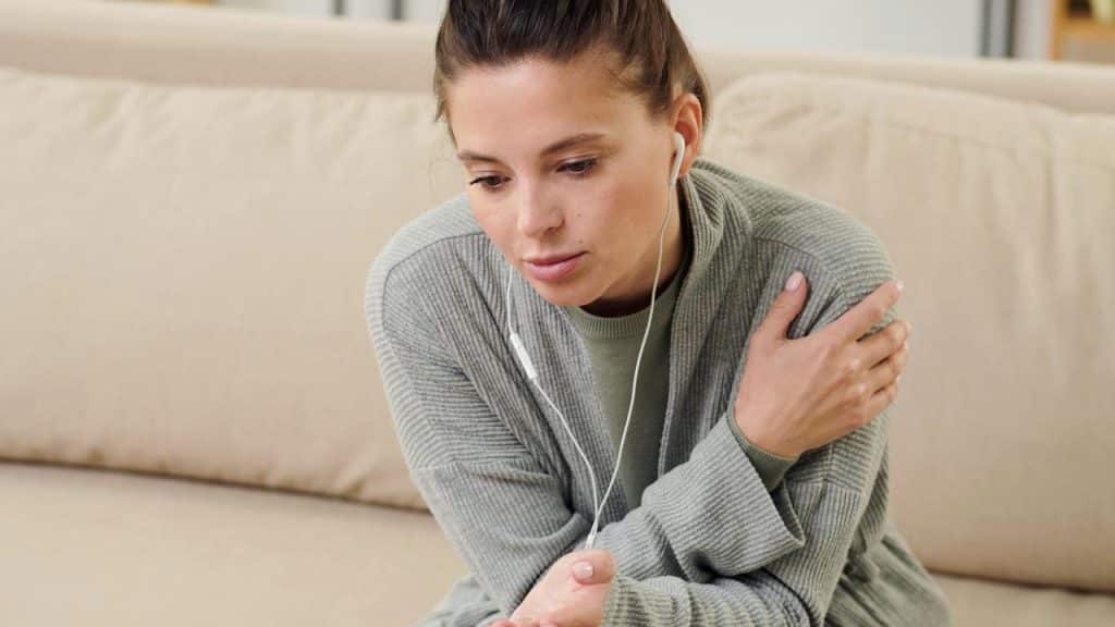 A woman wearing earphones looking down thoughtfully while sitting on a couch.