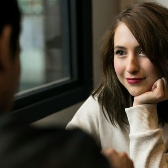 A woman with a slight smile sits across from a person, resting her chin on her hand.