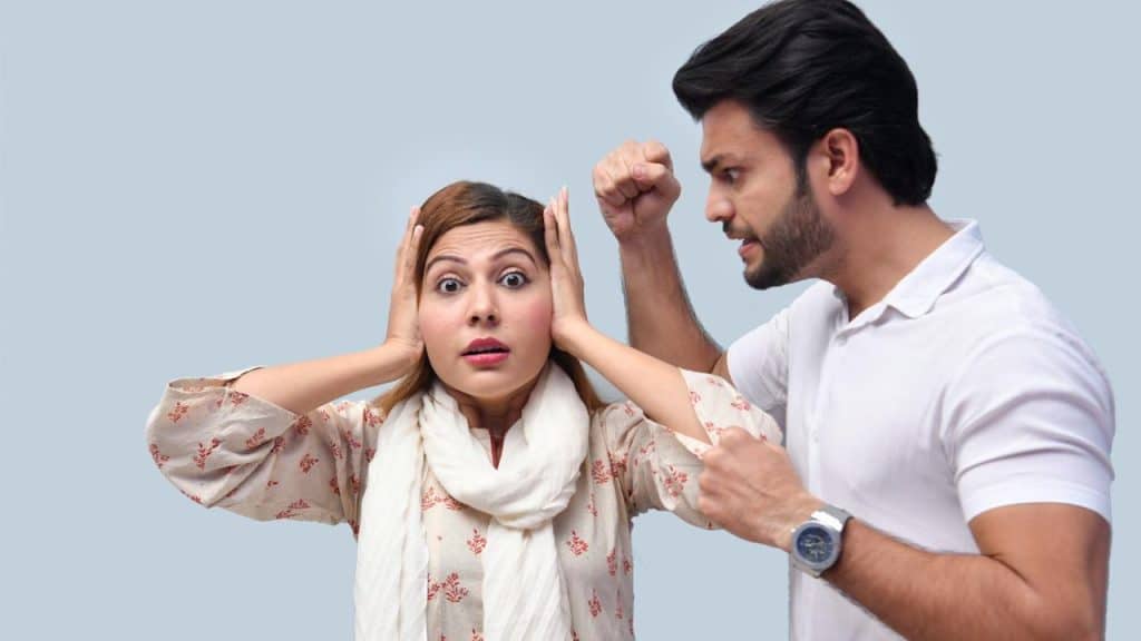 A man screaming and showing a fist bump to his wife, who is covering her ears with her hands while standing next to him.