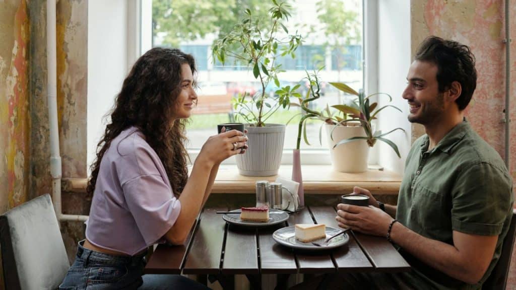 A smiling couple enjoys coffee and cake at a cafe table.
