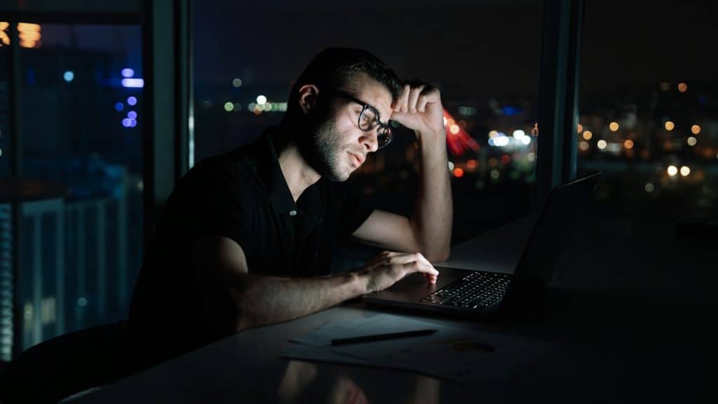 A man sitting at a dark place is working on laptop.