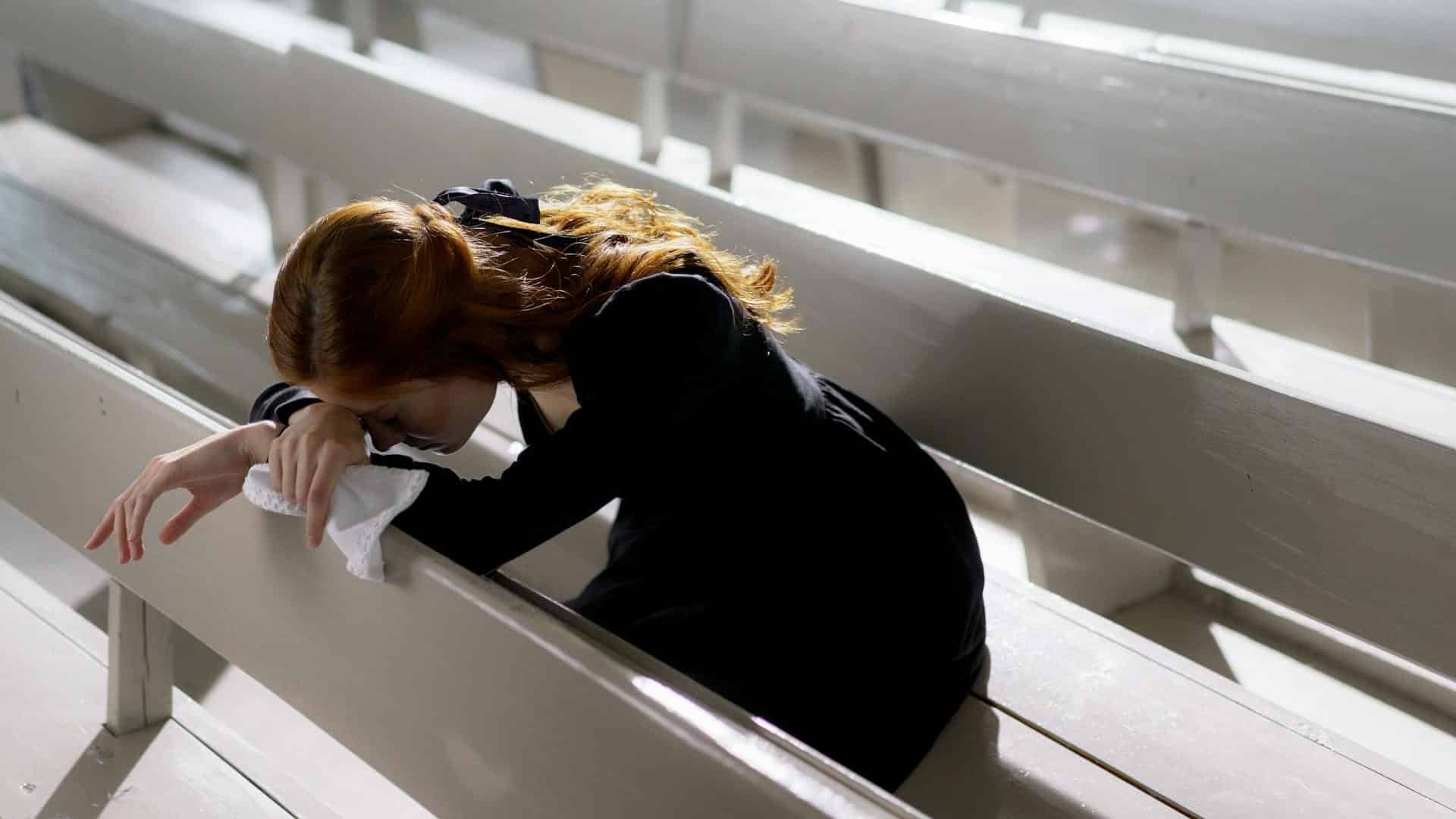 A sad woman sitting on wooden pew