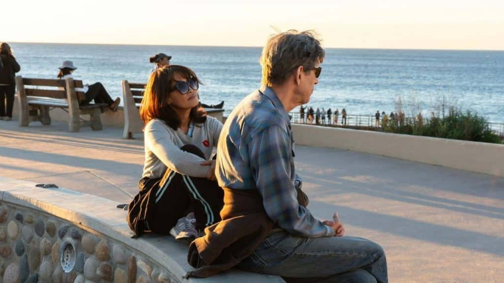 A man and woman sit on a stone wall overlooking the ocean at sunset.