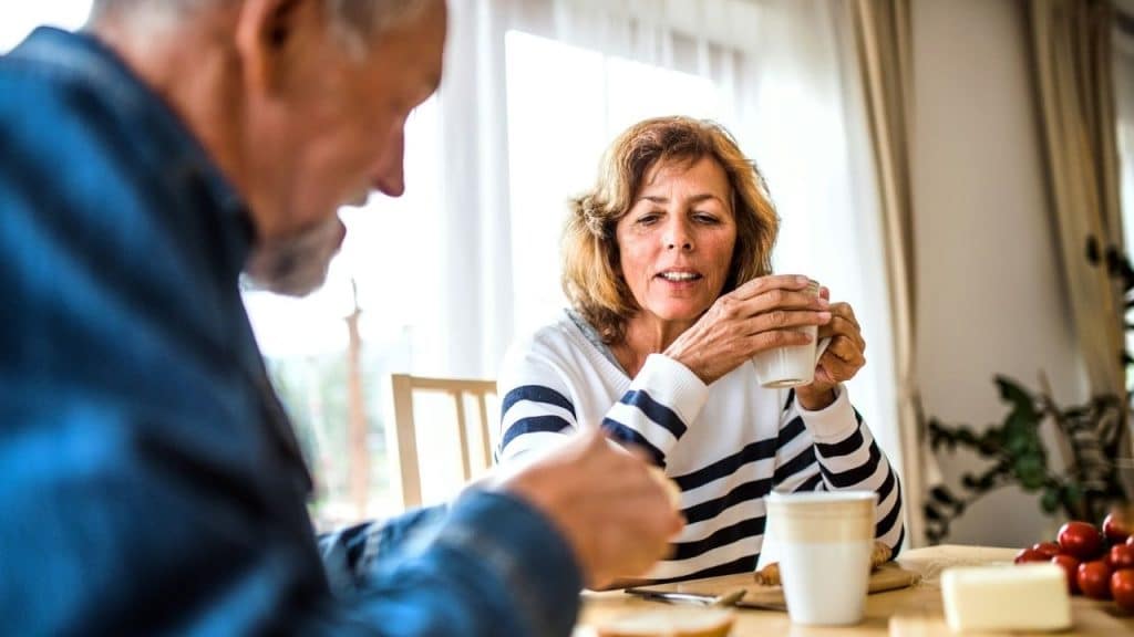 A woman in a striped shirt holds a mug while talking to a man at a table.