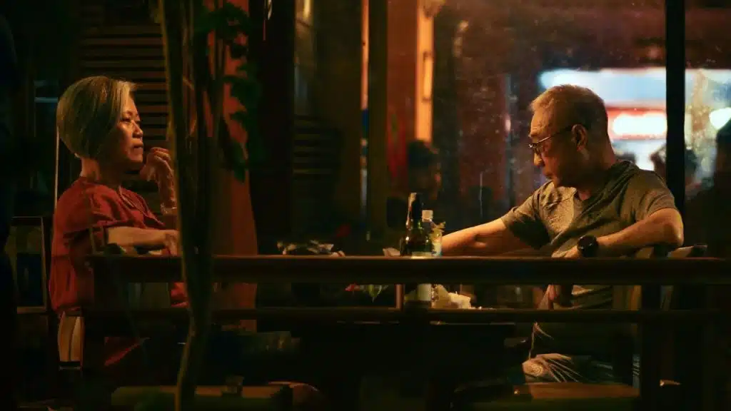 A man and woman sit at a dark wooden table in a dimly lit restaurant.