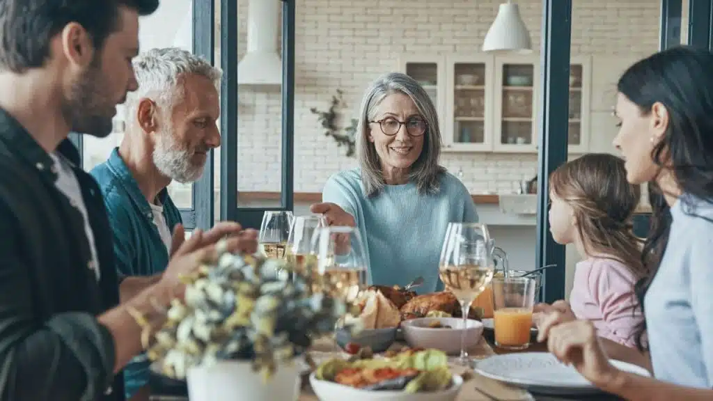 A multi-generational family sits around a dining table with food and wine glasses.