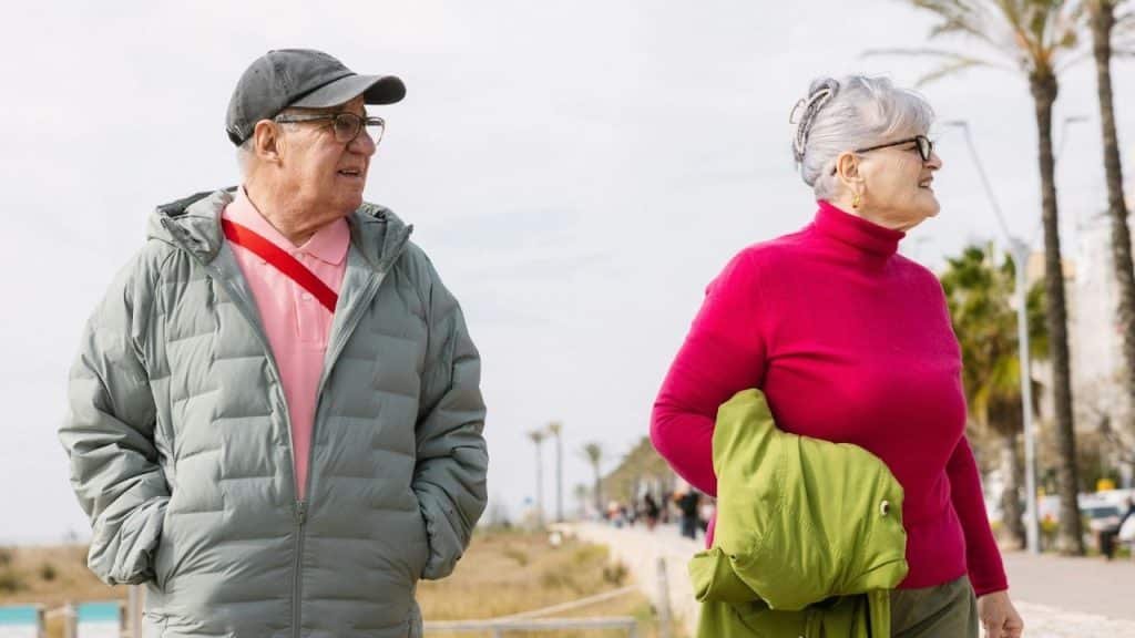 An older man and woman walk alongside each other outdoors on a bright day