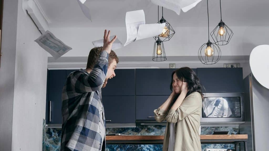 A man shouts while throwing papers into the air near a woman covering her ears.