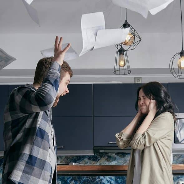 A man shouts while throwing papers into the air near a woman covering her ears.