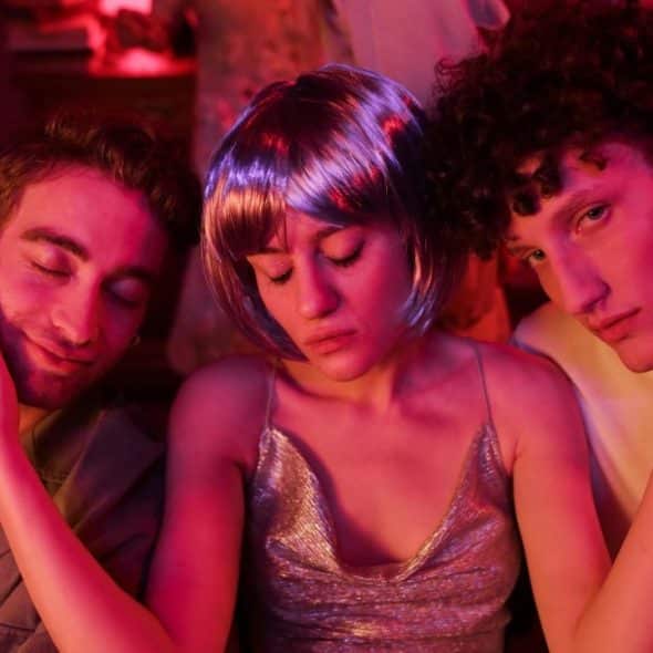 Three young people posing closely together under vibrant pink and purple neon club lighting.
