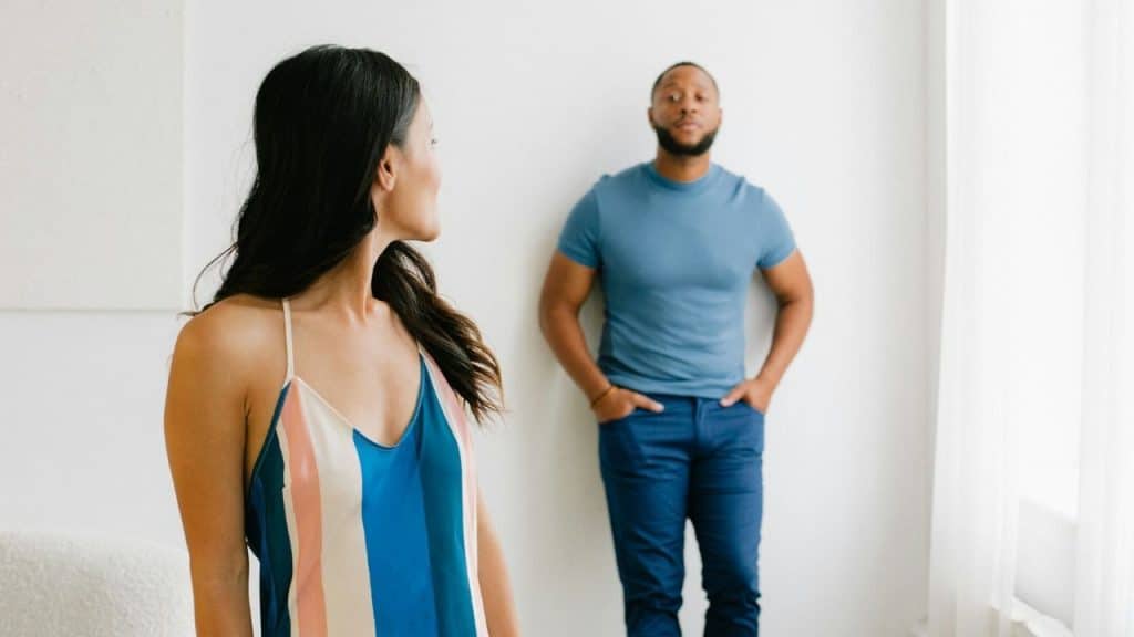 A woman stands looking at a man behind leaning the wall.