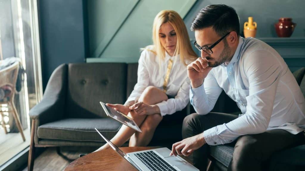 A man uses a laptop while a woman beside him looks at a digital tablet.