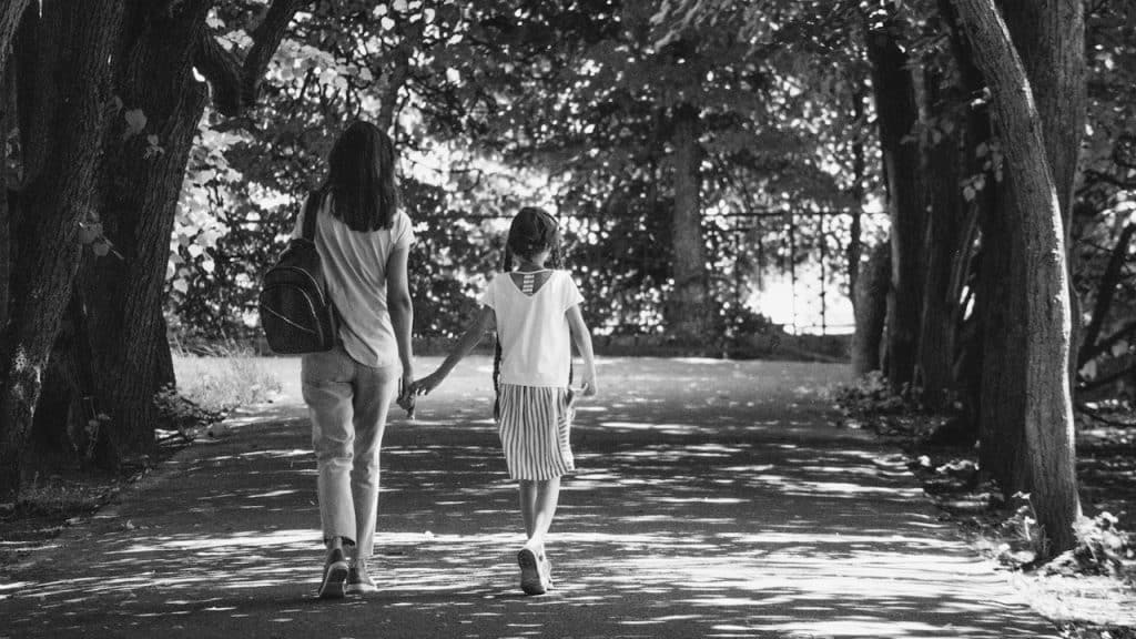 A woman and a girl walking down a path surrounded by trees.