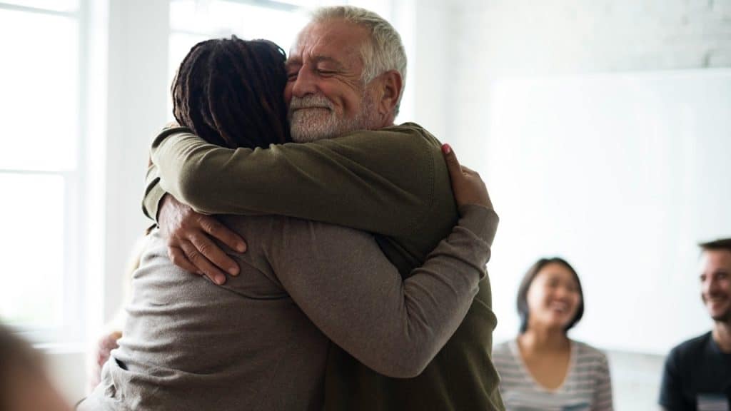 An older man hugging his wife while some people smile in the background