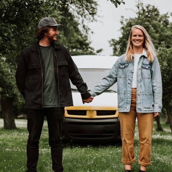 A couple holding hands while they are standing in a garden in front of a truck.