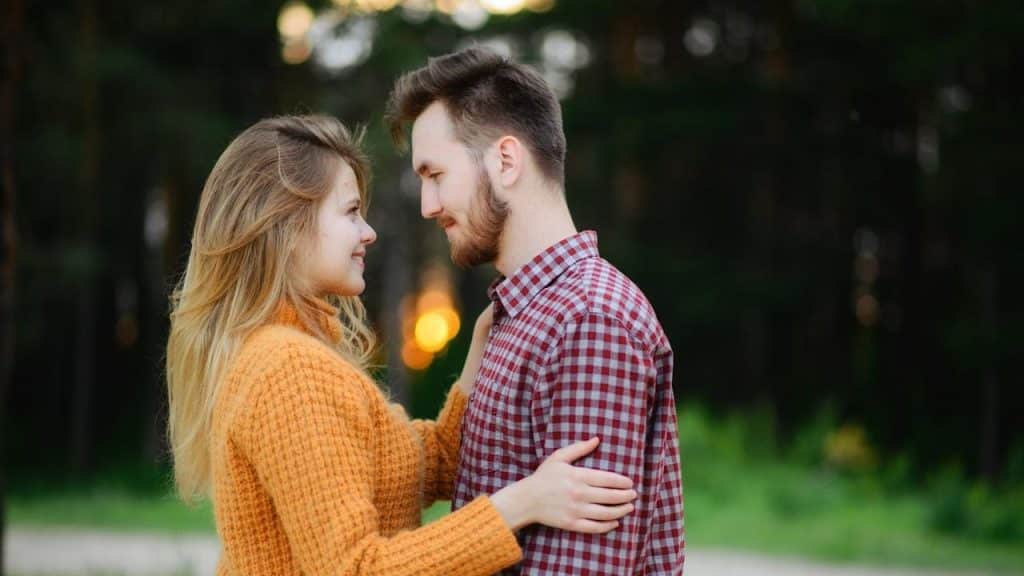 A man and woman facing each other while standing near a green field.