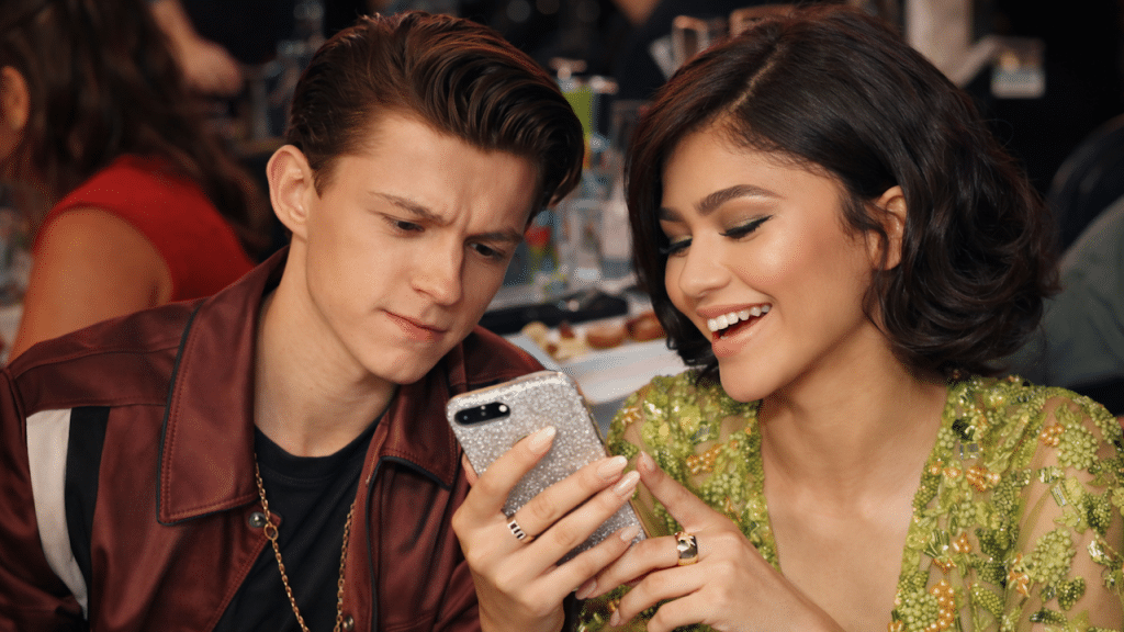 An image of Zendaya smiling and showing Tom Holland something on her phone.