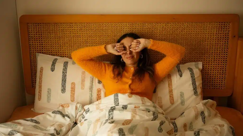 A woman in bed rubbing her eyes as she wakes up.