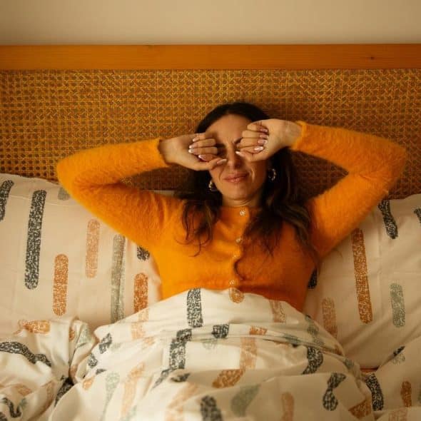 A woman in bed rubbing her eyes as she wakes up.