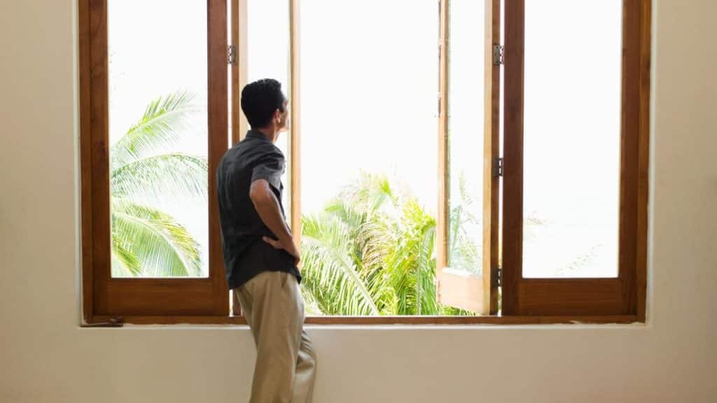 A man standing by an open window looking outside.