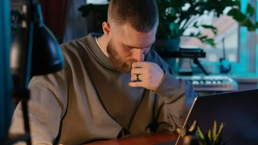 A man sitting at a desk looking down thoughtfully beside a laptop.