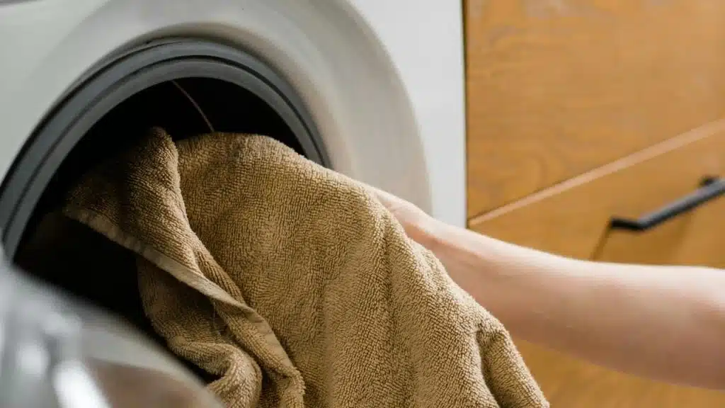 A person placing a towel into a washing machine.