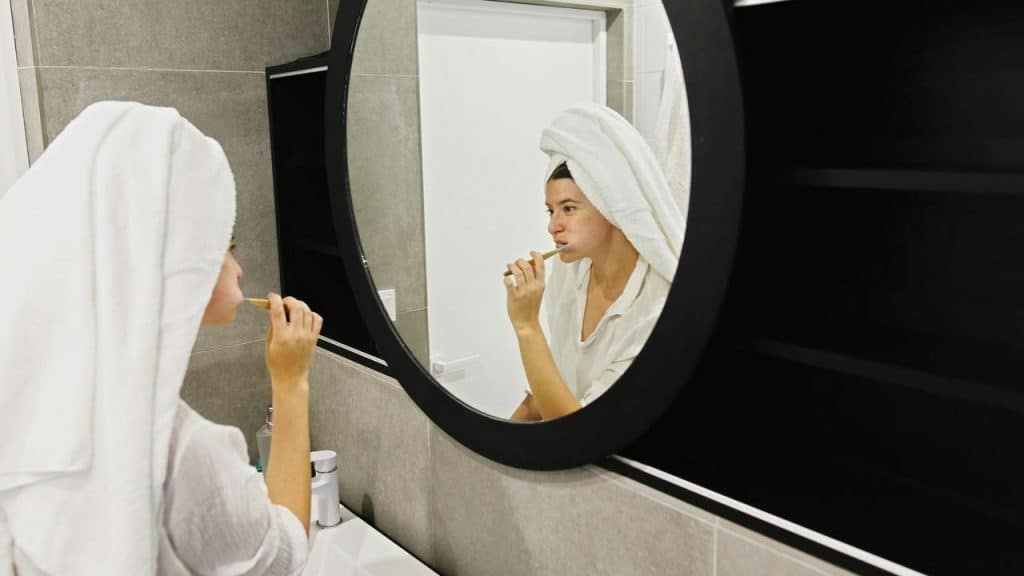 A person brushing their teeth in a bathroom mirror.