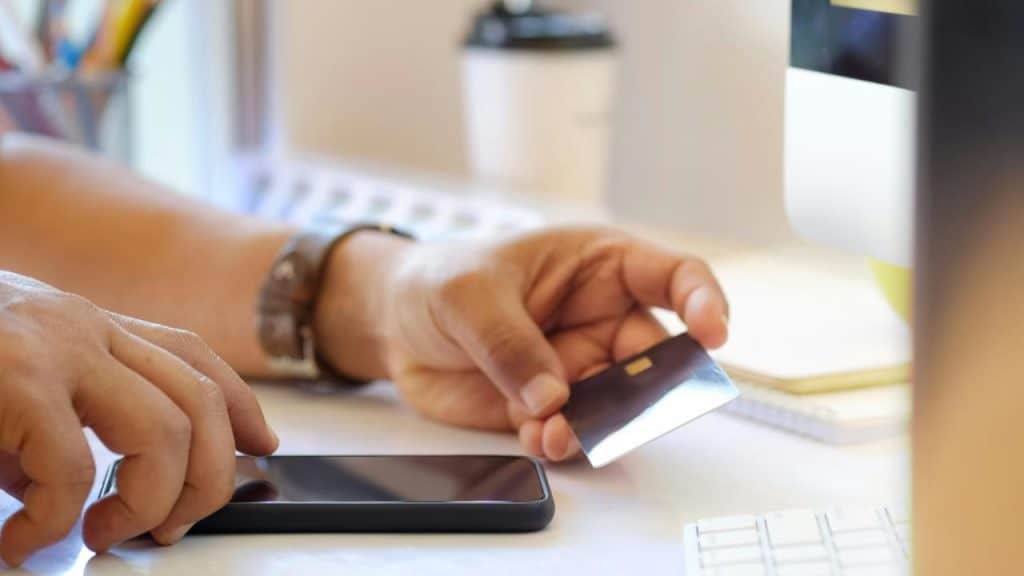 A person holding a credit card and smartphone at a desk.