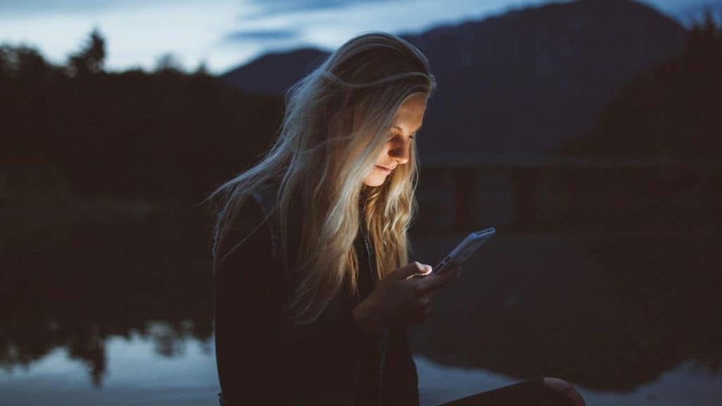 A woman outdoors at dusk looking at her phone.