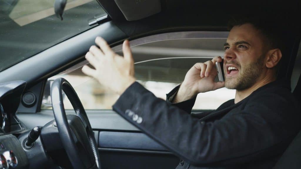 A man driving a car while talking on his phone and gesturing.