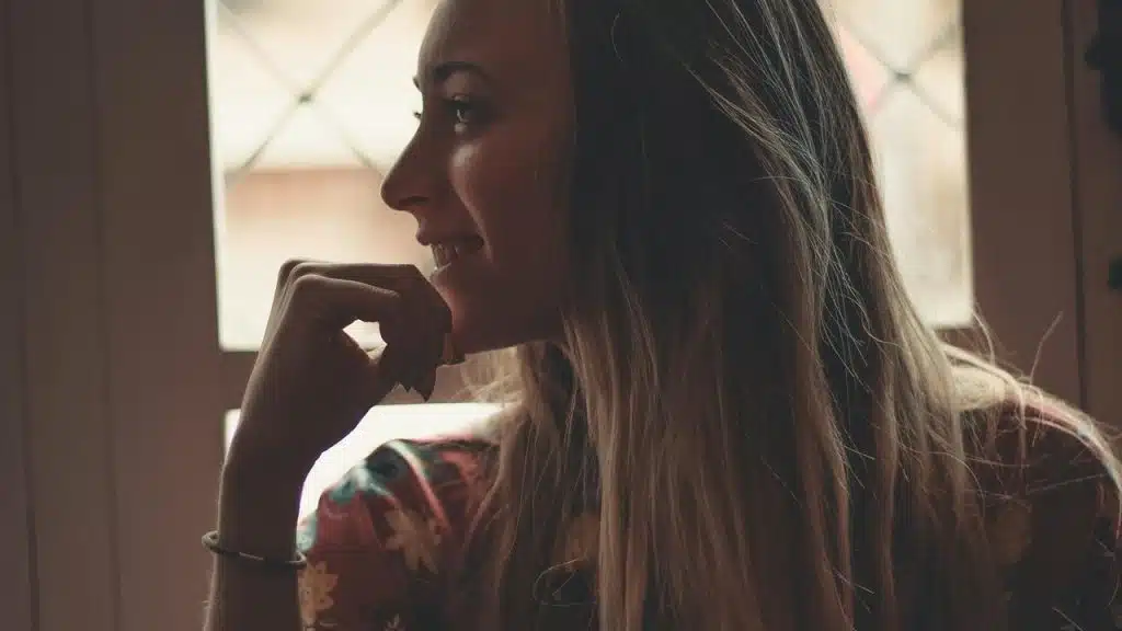 A woman smiling thoughtfully while looking out a window.