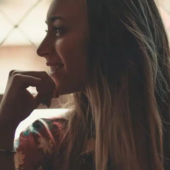 A woman smiling thoughtfully while looking out a window.